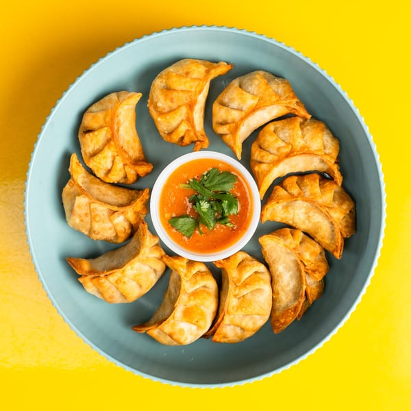 Fried Momo House dumplings arranged in a circle around a small bowl of orange dipping sauce with cilantro.