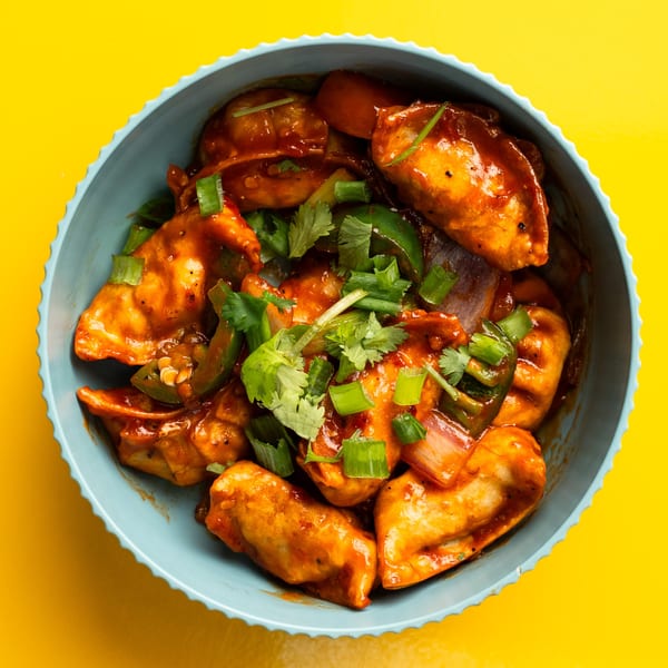 A blue bowl filled with Momo House San Antonio's chili momos, garnished with green onions and cilantro.