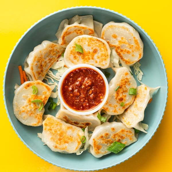 Pan-fried Momo House dumplings with spicy red chili sauce, cabbage, and carrots in a blue bowl.