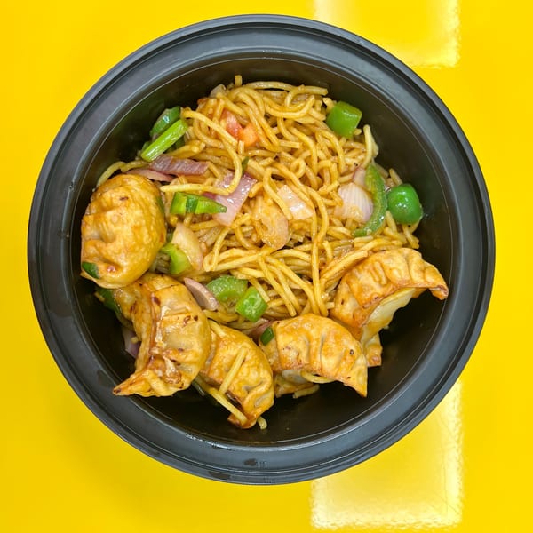 Momo House San Antonio's chili garlic noodles with fried momos, green peppers, and onions in a black bowl.
