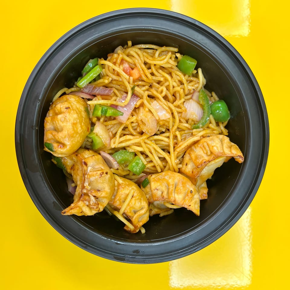 Momo House San Antonio's chili garlic noodles with fried momos, green peppers, and onions in a black bowl.