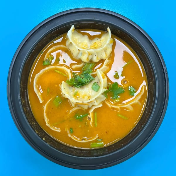 Overhead view of Nepali momo dumplings in a rich orange broth, garnished with fresh cilantro.
