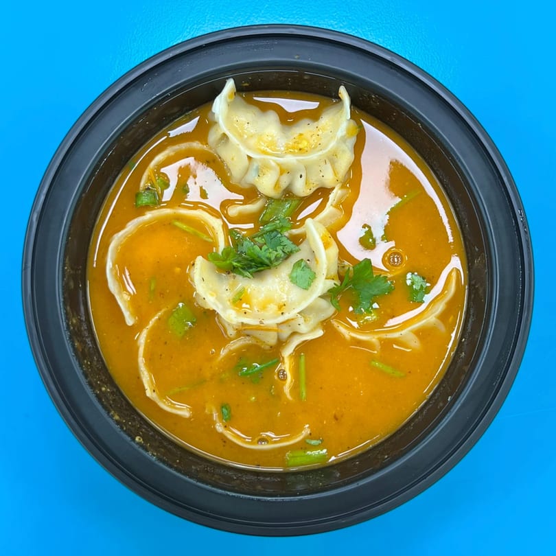 Overhead view of Nepali momo dumplings in a rich orange broth, garnished with fresh cilantro.