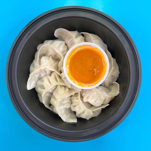 A black bowl of Momo House San Antonio dumplings with a small cup of orange dipping sauce.