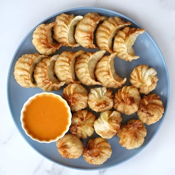 A blue plate filled with crispy fried Nepali momo dumplings and a side of orange dipping sauce.